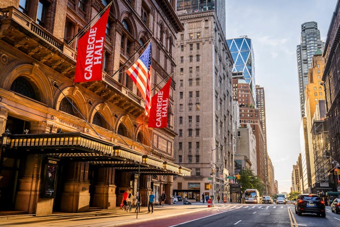The street outside Carnegie Hall during the day, red banners flying above the hall