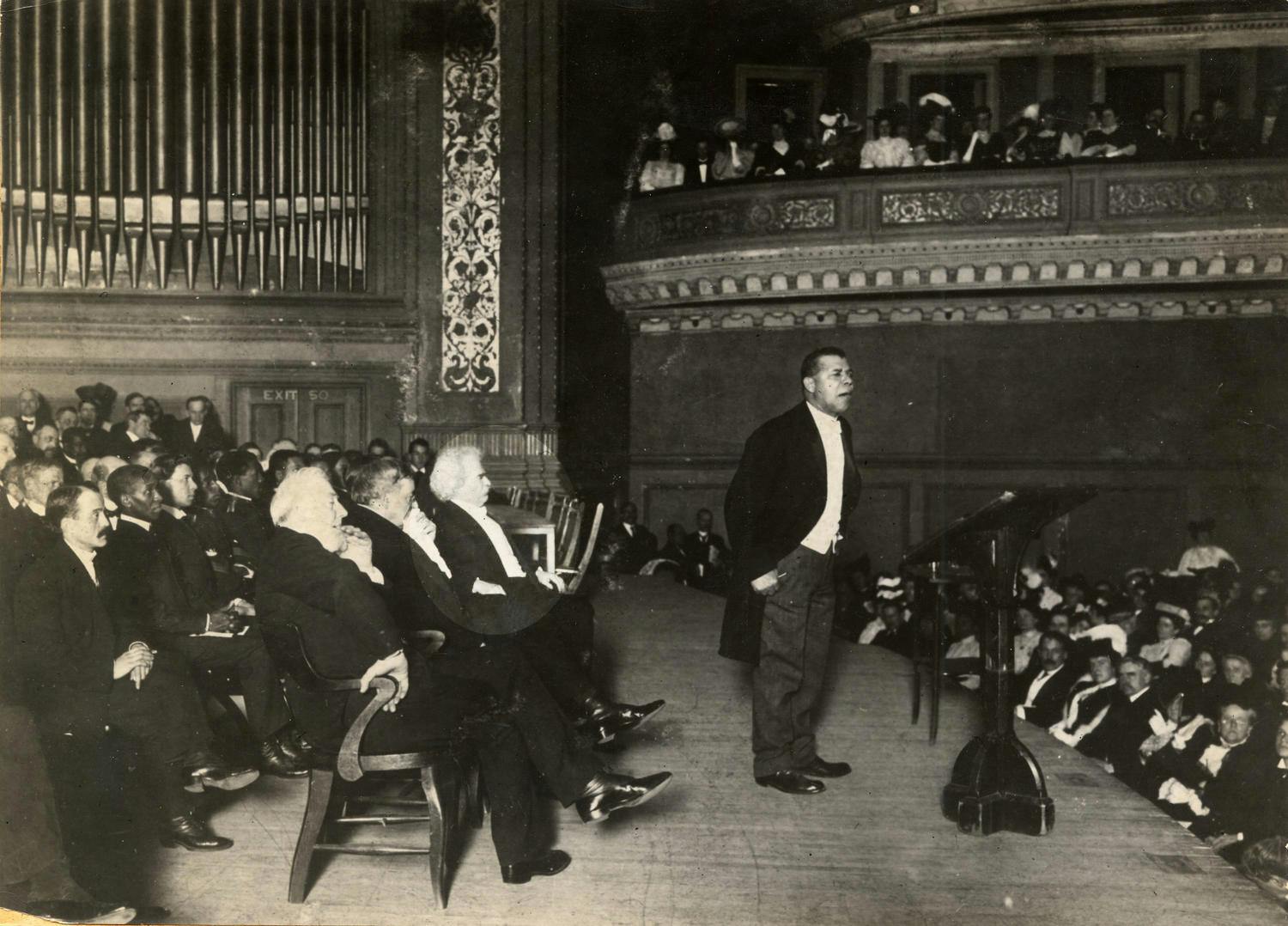 Mark Twain seated on stage behind Booker T. Washington, 1906