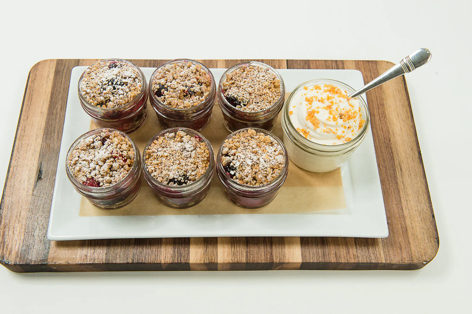 Six cups of apple crisp on a cutting board with a cup of whipped cream on the side