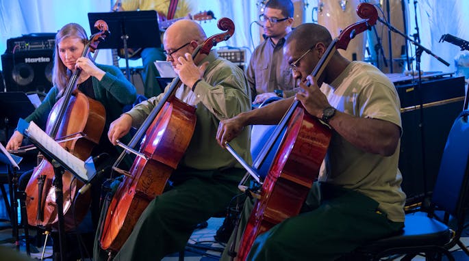 Two men and a woman play the cello with backup musicians at Sing Sing Correctional Facility.