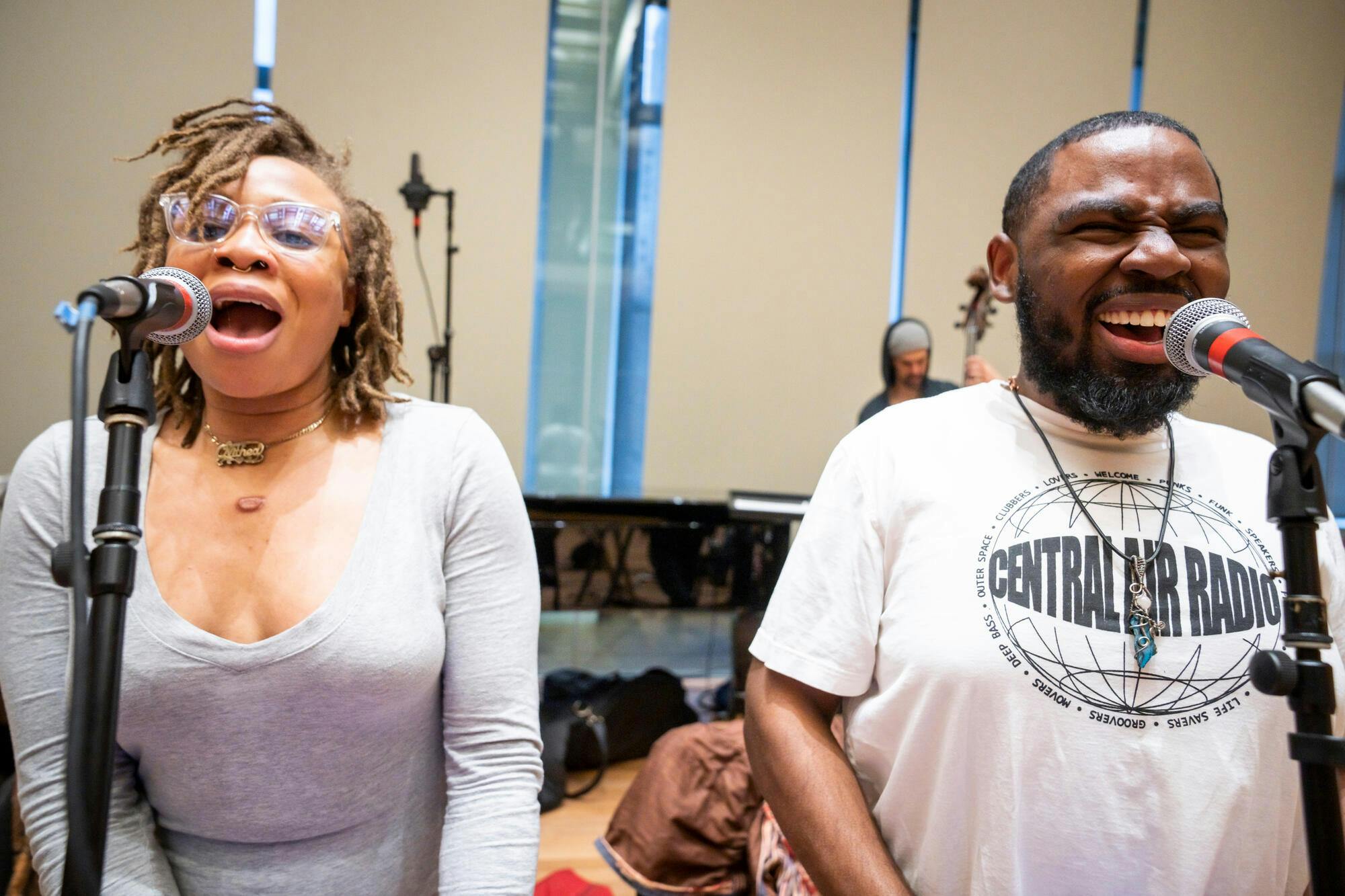 A woman and a man sing into microphones in a studio