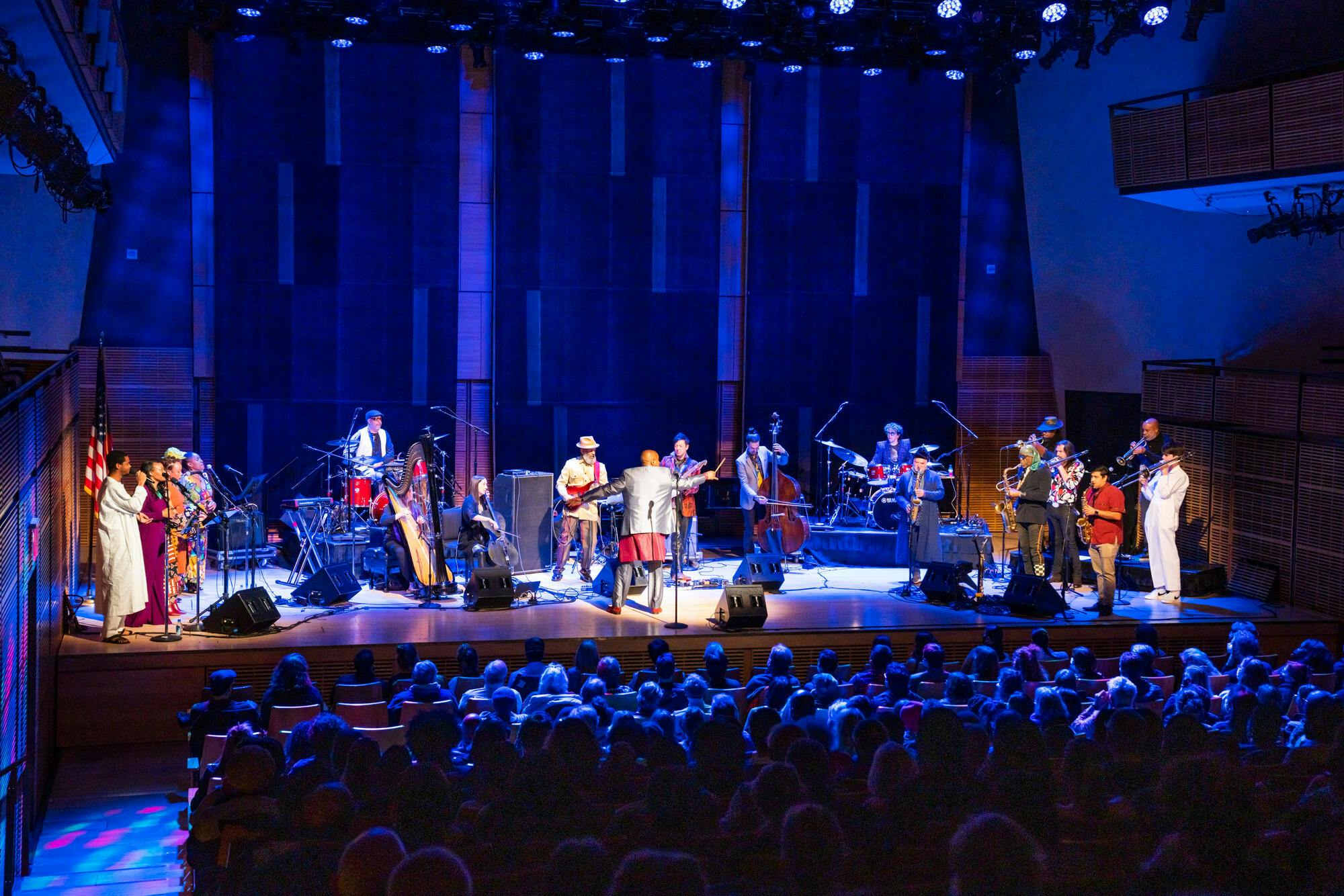 An audience watches as an orchestra performs under blue lighting