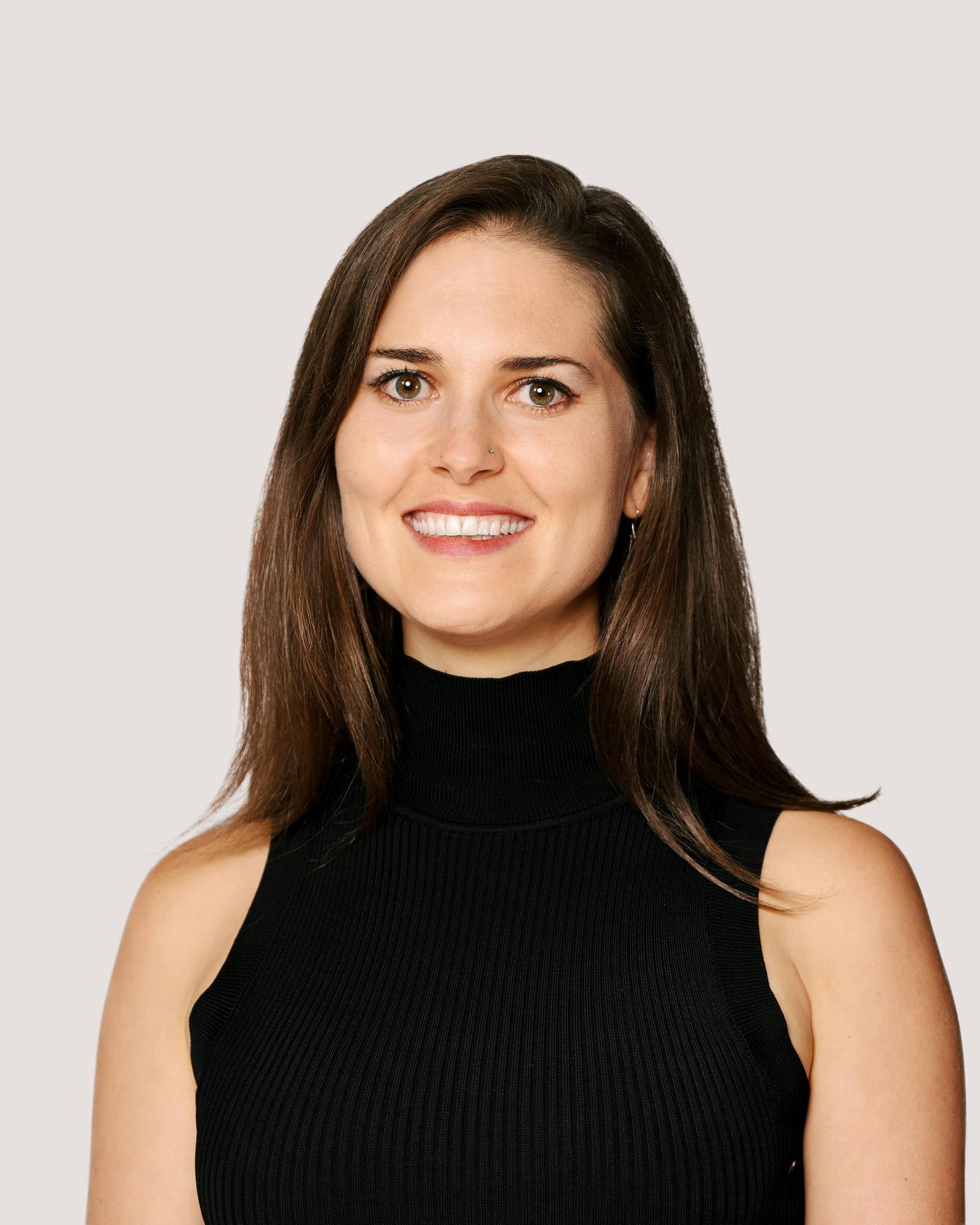 young woman in a black sleeveless turtleneck sweater with brown hair and eyes smiles.