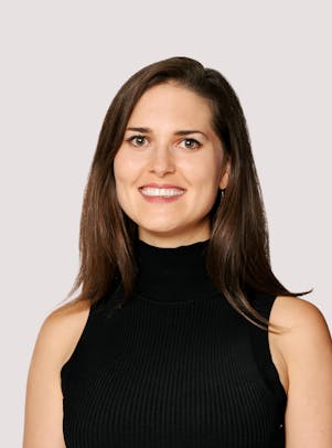  young woman in a black sleeveless turtleneck sweater with brown hair and eyes smiles.