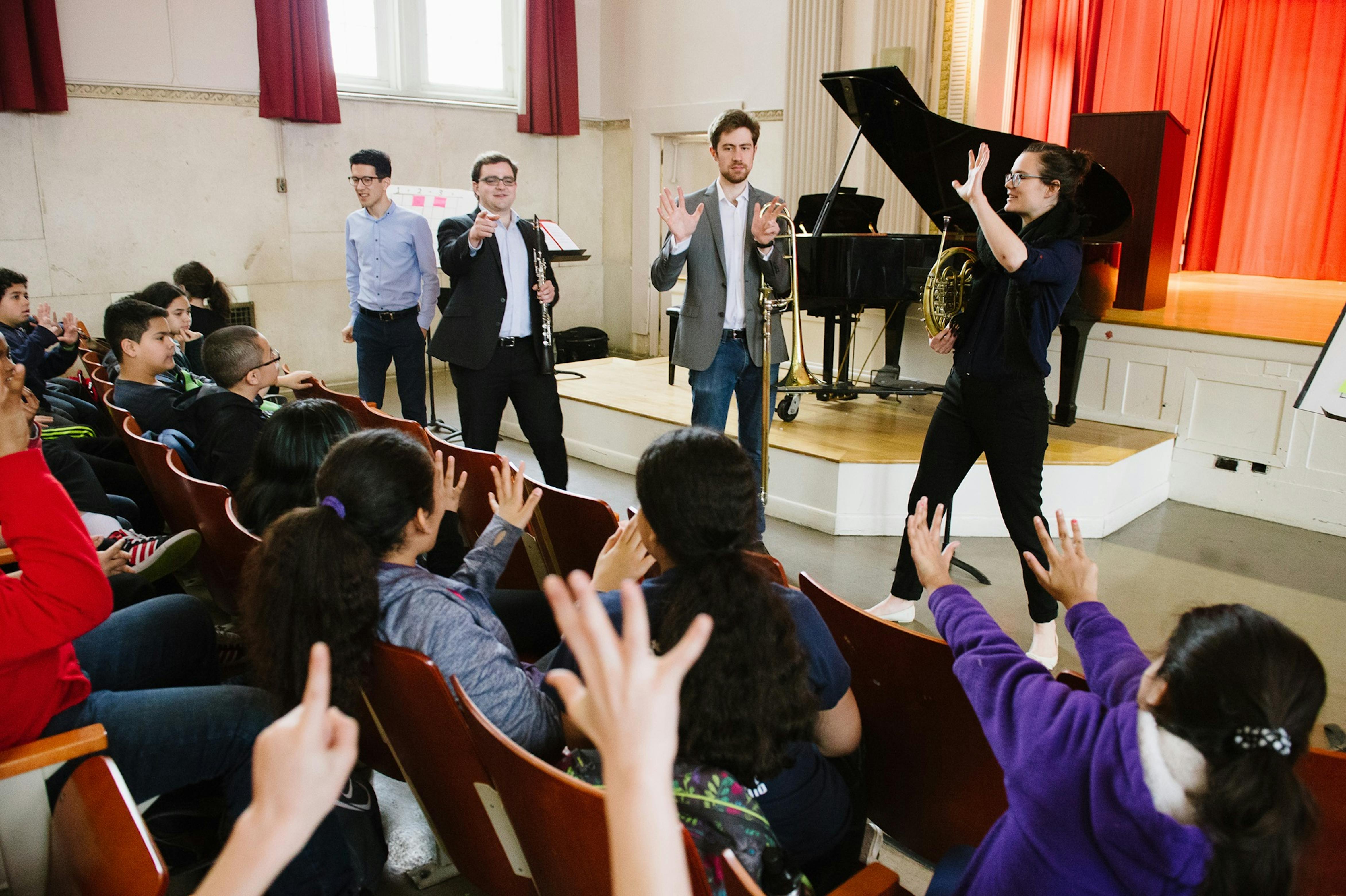 Musicians hold instruments and answer questions from schoolchildren in an auditorium
