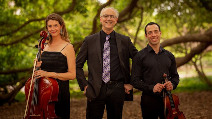 Musicians of Congaree Trio pose together with their instruments on a wooded path