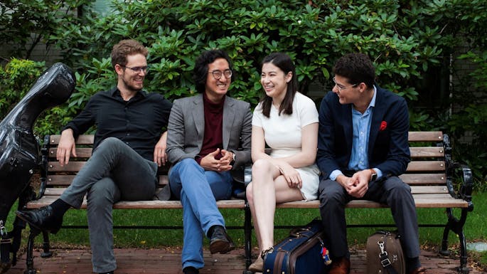 Musicians of Ensemble132 sit together on a bench