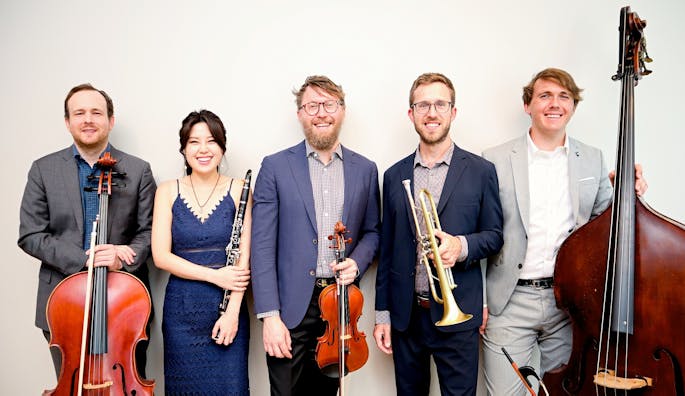 Four men and one woman in formal attire stand together smiling, holding various instruments.