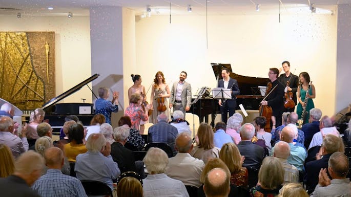 A group of musicians stand before a small audience in a gallery