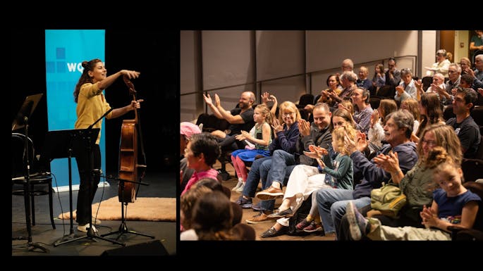A smiling woman holding a cello gestures toward an applauding audience