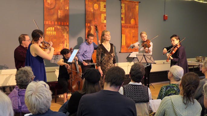 A group of instrumentalists and a singer perform for a seated audience.