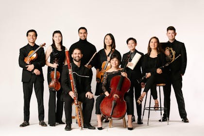 A group of young musicians pose with their instruments against a white backdrop.