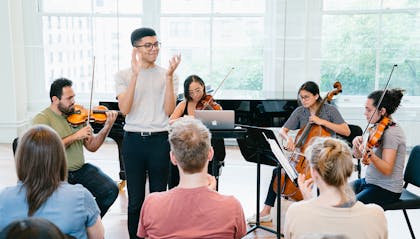 A string quartet plays as a young man in glasses claps in front of an audience.