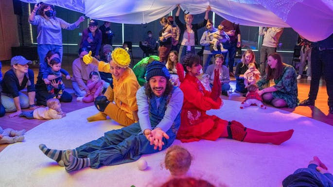 Men and women in colorful outfits interacting with toddlers.