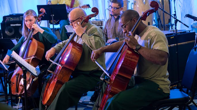 Two men in glasses and green pants and a woman play the cello at Sing Sing Correctional Facility.