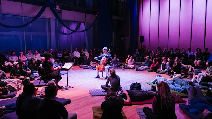 People laying on mats surrounding a cellist