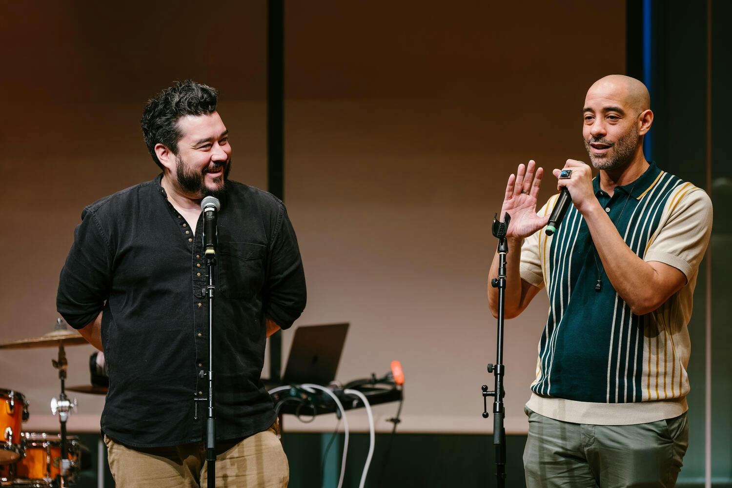 One man watches, laughing, as another man speaks into a mic