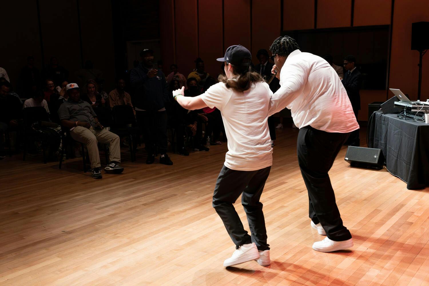Two young men wearing black pants and white shirts perform before an audience