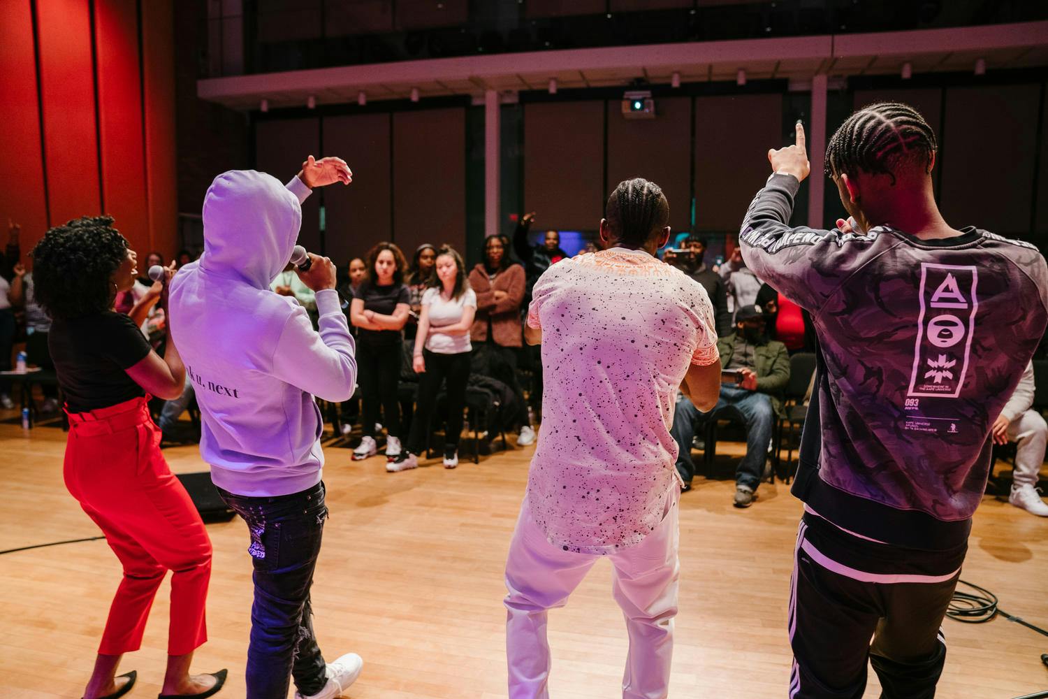 Three young men and a young woman sing into mics before an audience