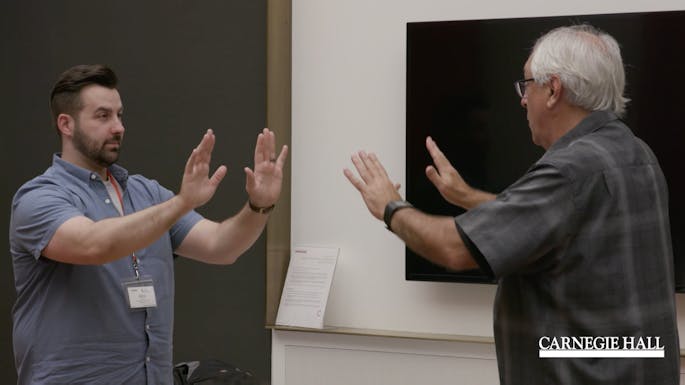A presenter and a teacher hold up their hands toward each other