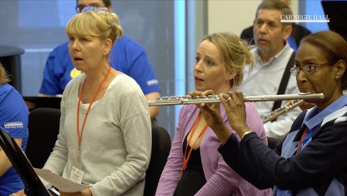 A group of teachers sing as a flutist plays