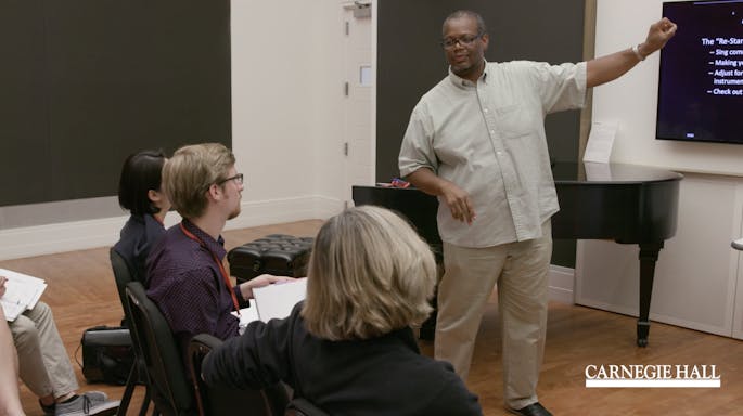 A man speaks before a group of teachers in a workshop