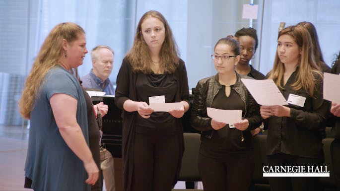 A group of young students listen as a teacher guides them through an exercise
