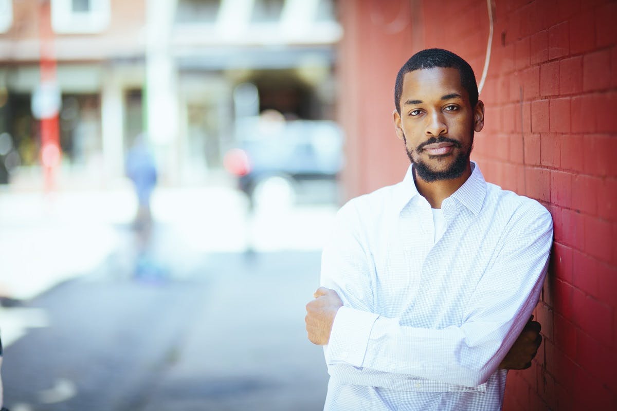 Elijah J. Thomas leaning against a red brick wall