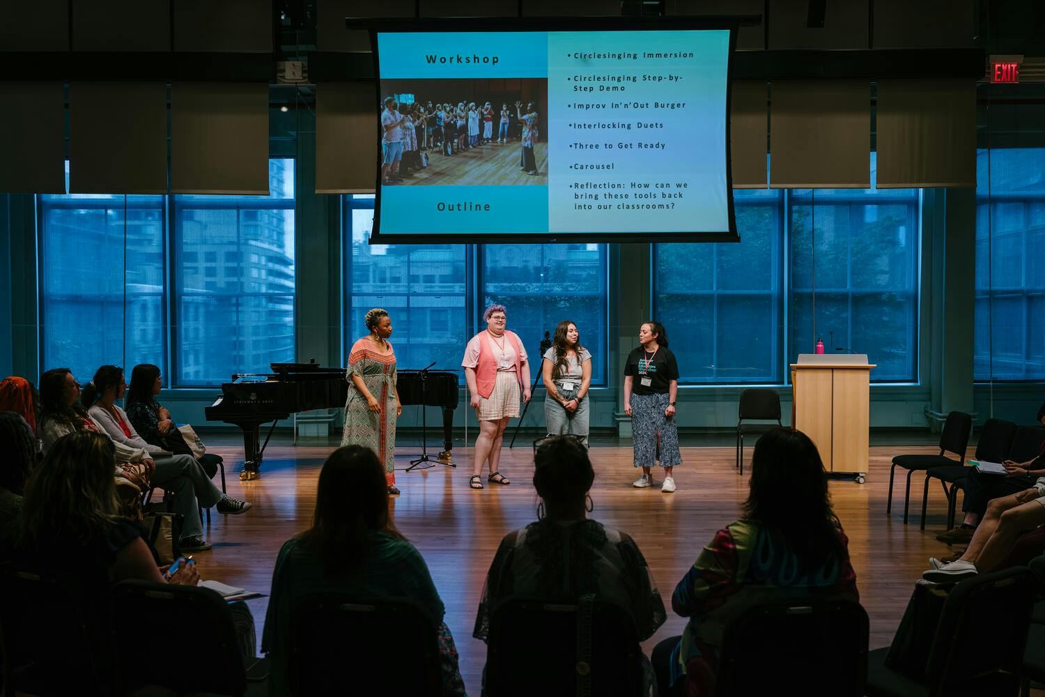 Four workshop teachers stand beneath a projection screen, before a small audience