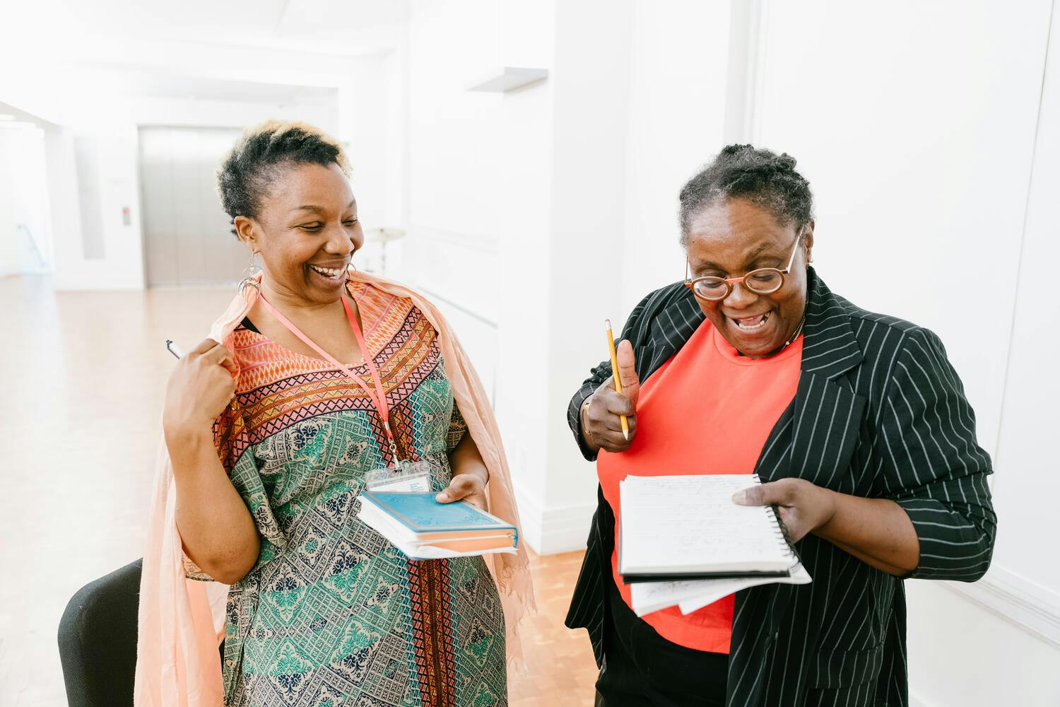 Two women laugh together as they look over a notebook