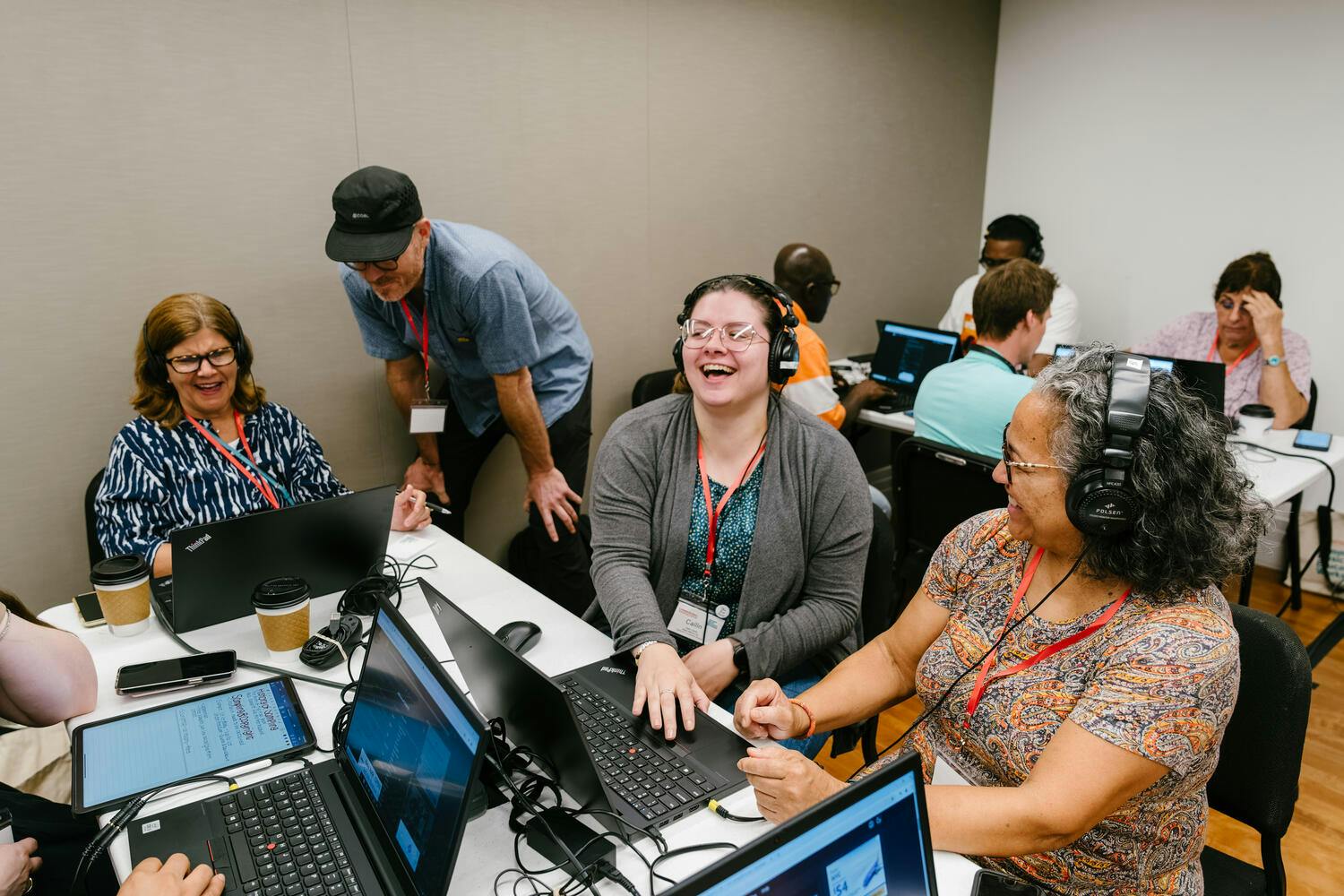 Two women laugh together over a PC as a young man instructs another woman on a PC