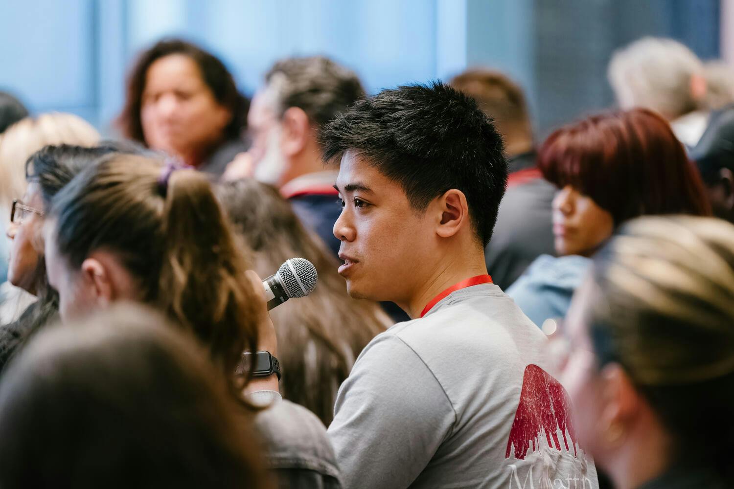 A young man speaks into a microphone, surrounded by other audience members