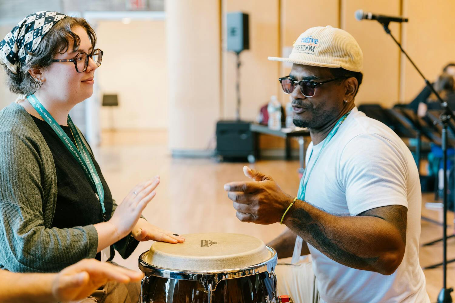A woman plays a drum as a man instructs her