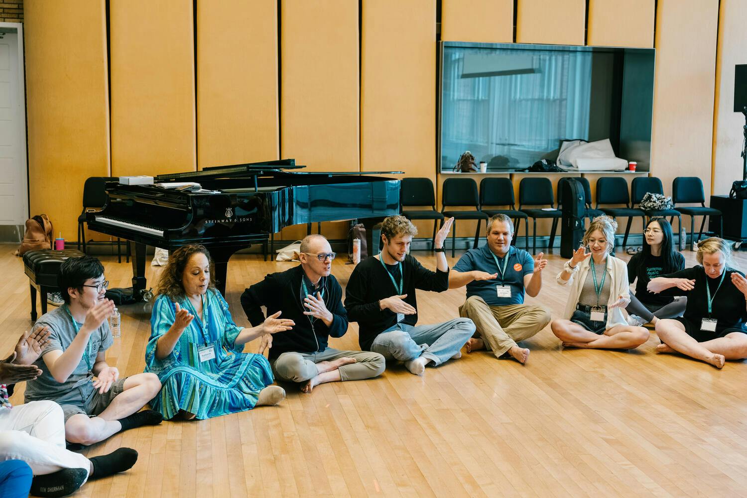 Men and women sit in a semi-circle, hands outstretched or upraised