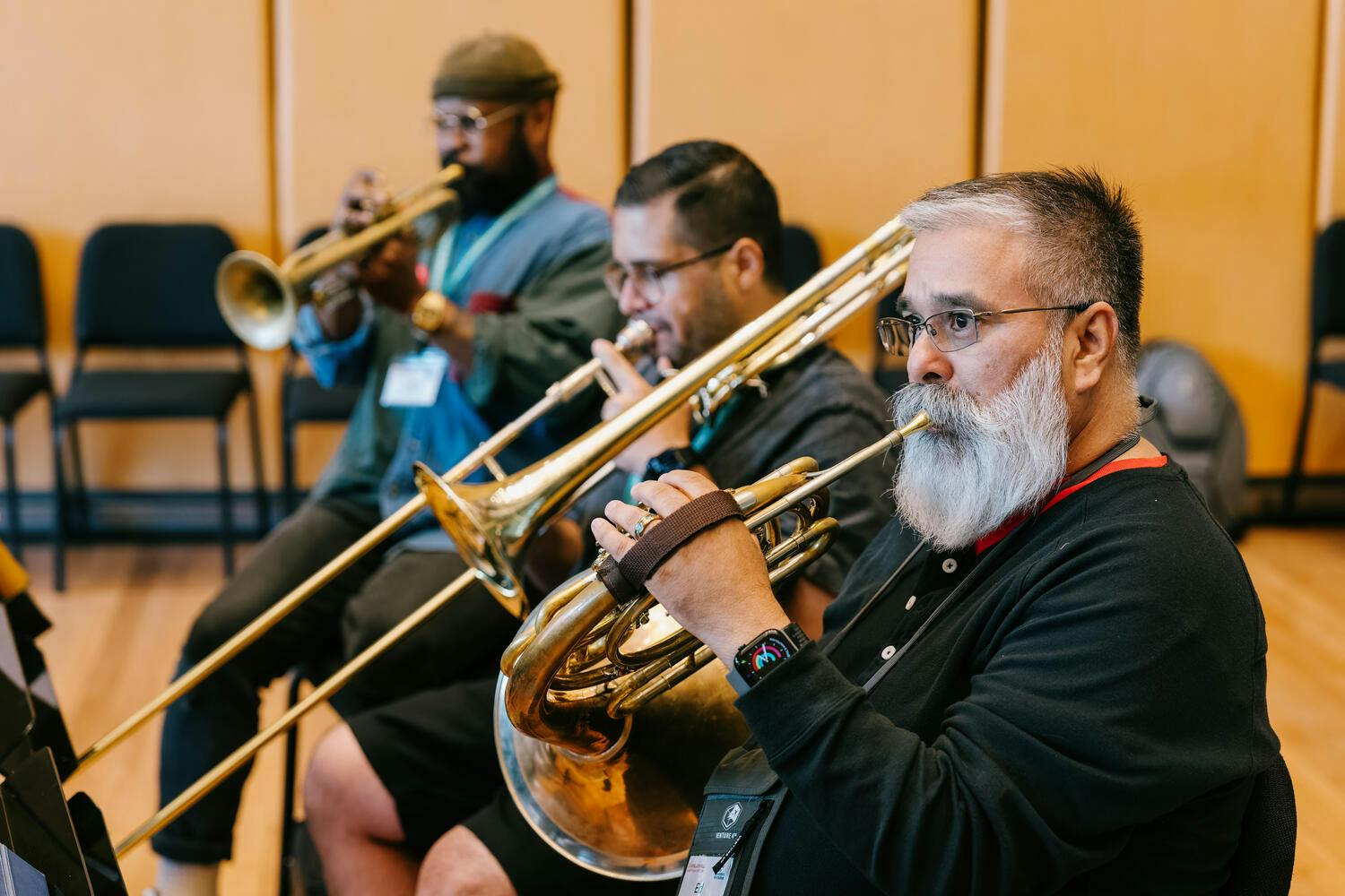 Three men seated play trumpet, trombone, and horn