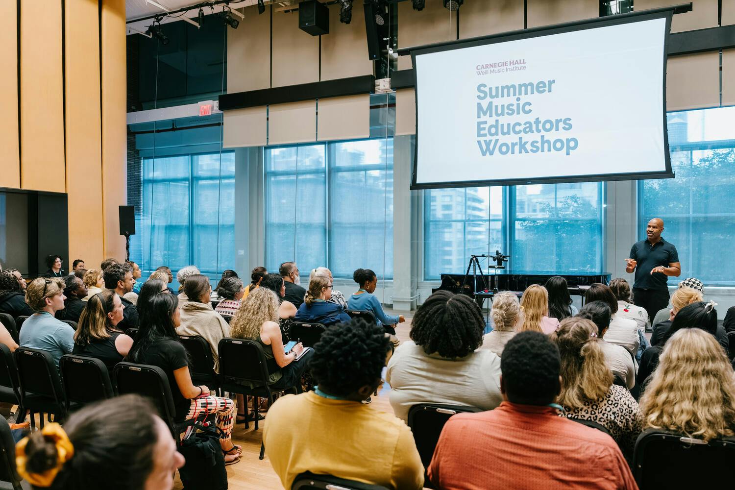 An audience watches as a man gives a presentation in a rehearsal studio