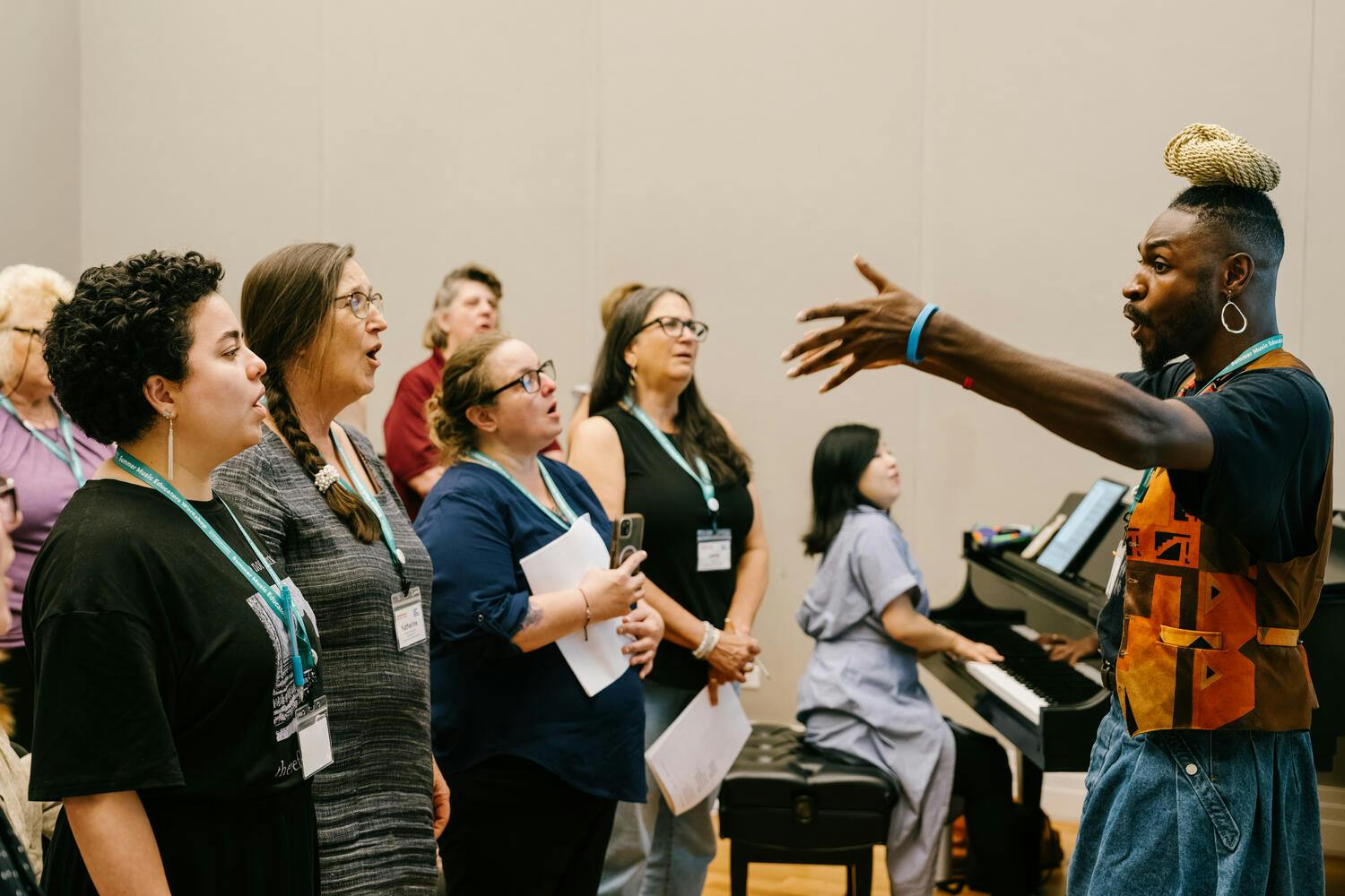 A man guides a choir as a woman plays piano