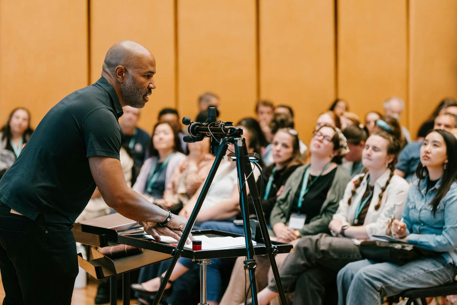A man speaks before an audience in a rehearsal studio