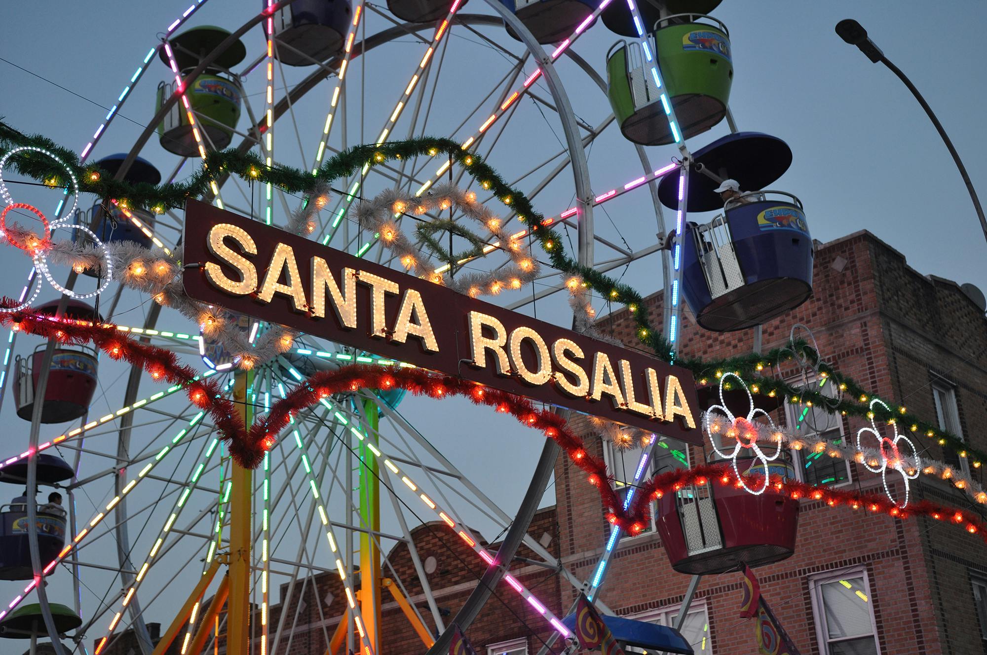 A sign that reads "Santa Rosalia" with a brightly lit ferris wheel behind it