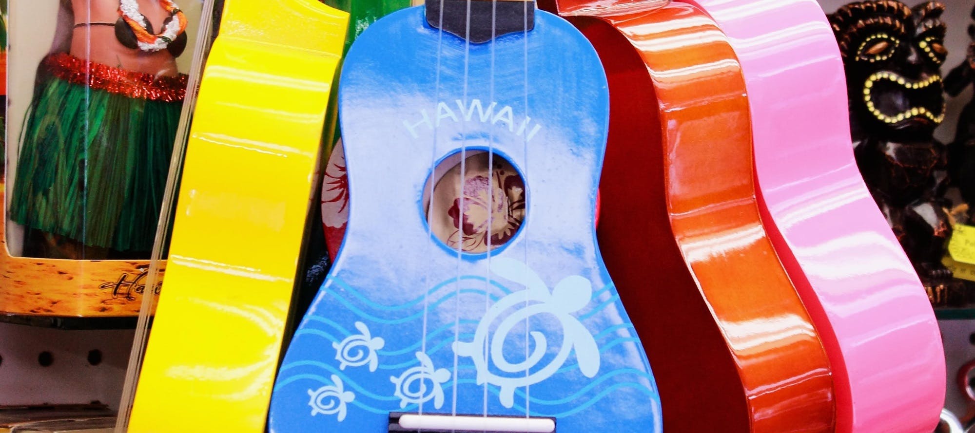 Yellow, blue, red, and pink guitars hang near a packaged hula doll