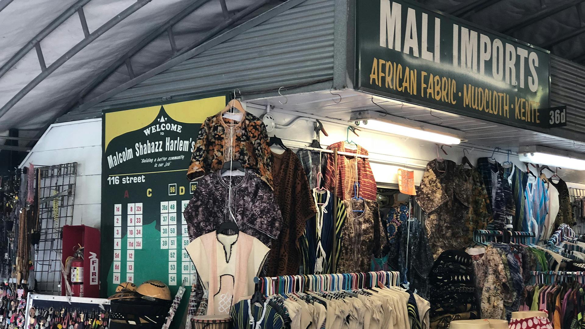 Various shirts hang from racks in a market with a sign that reads "Mali Imports African Fabric"