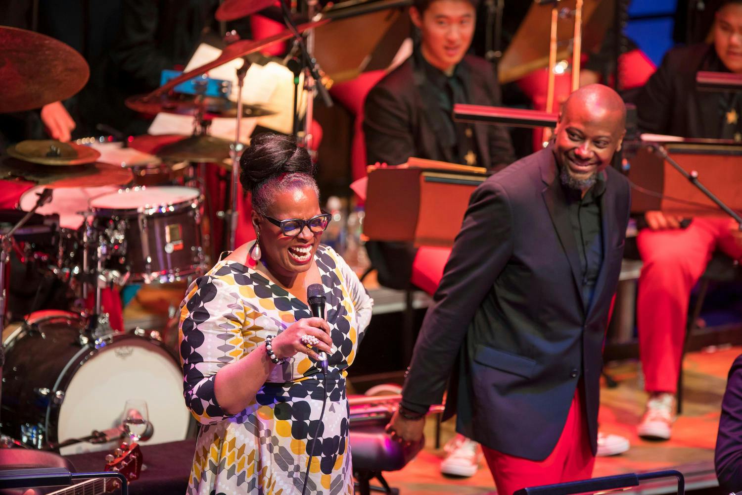 Dianne Reeves sings into a microphone on stage as Sean Jones looks on