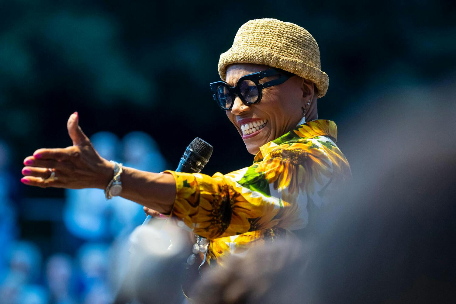 Smiling Dee Dee Bridgewater, left hand outstretched as she holds a microphone