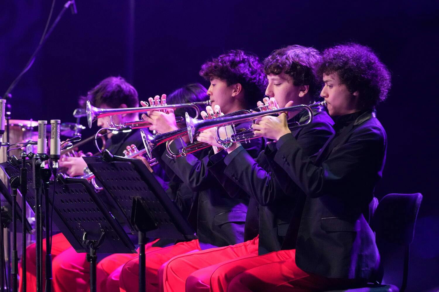 NYO Jazz trumpeters perform on stage, wearing red pants and black jackets