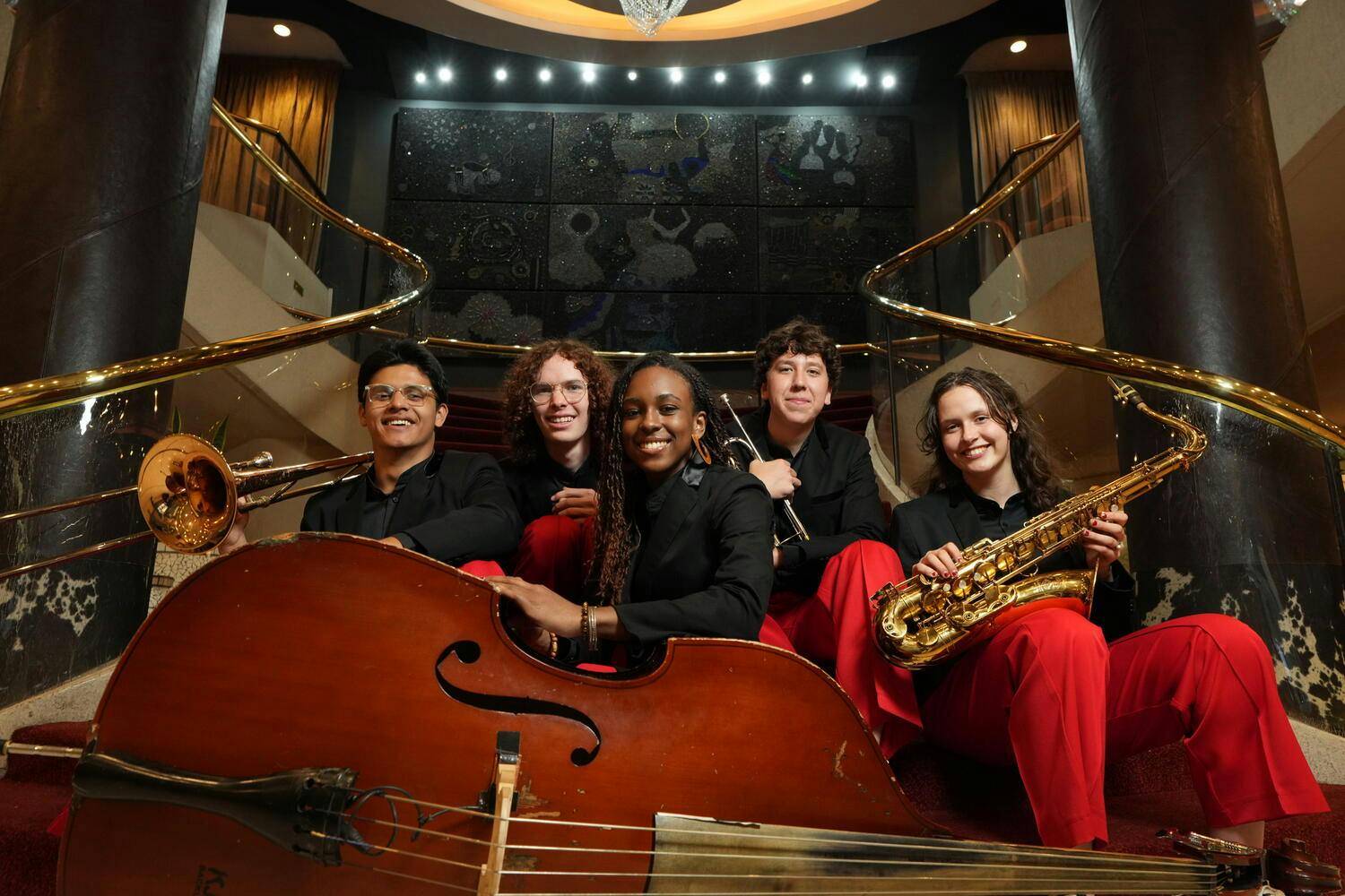 NYO Jazz musicians pose together on a staircase before a giant string bass