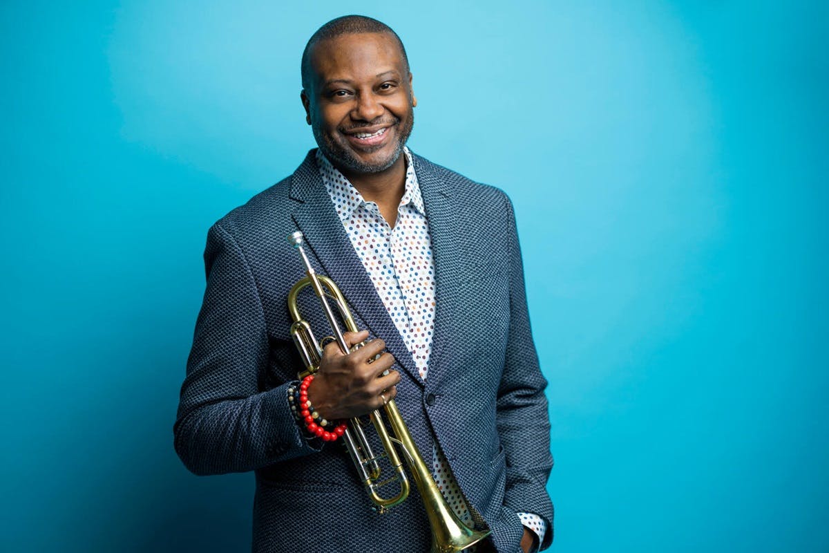 Smiling Sean Jones with trumpet against a light blue background