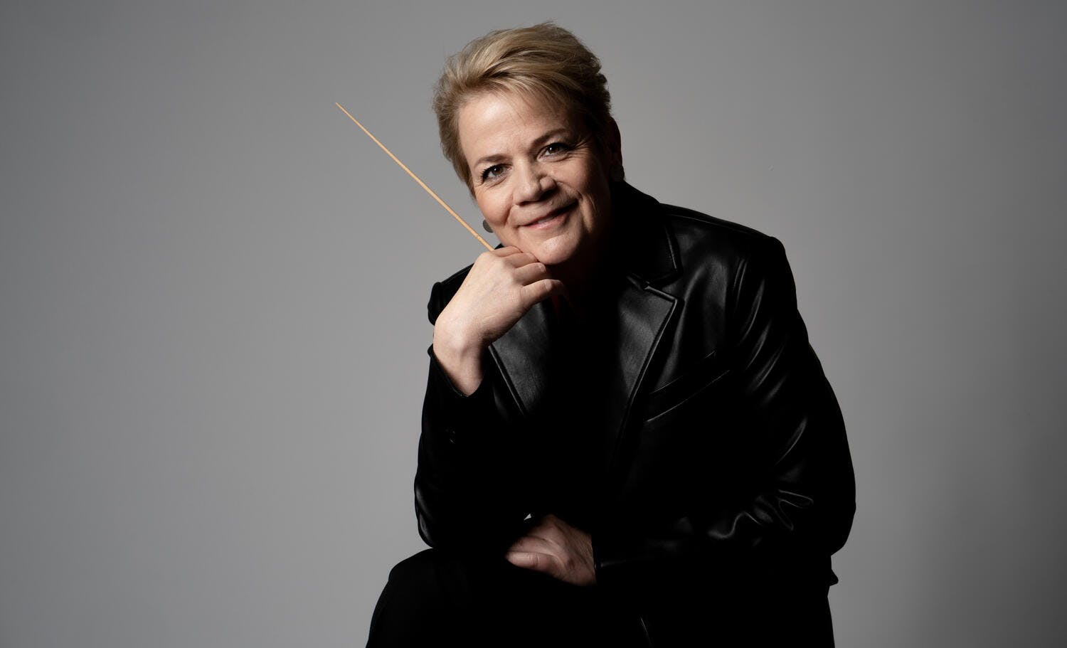 Marin Alsop wearing a black jacket, baton in hand