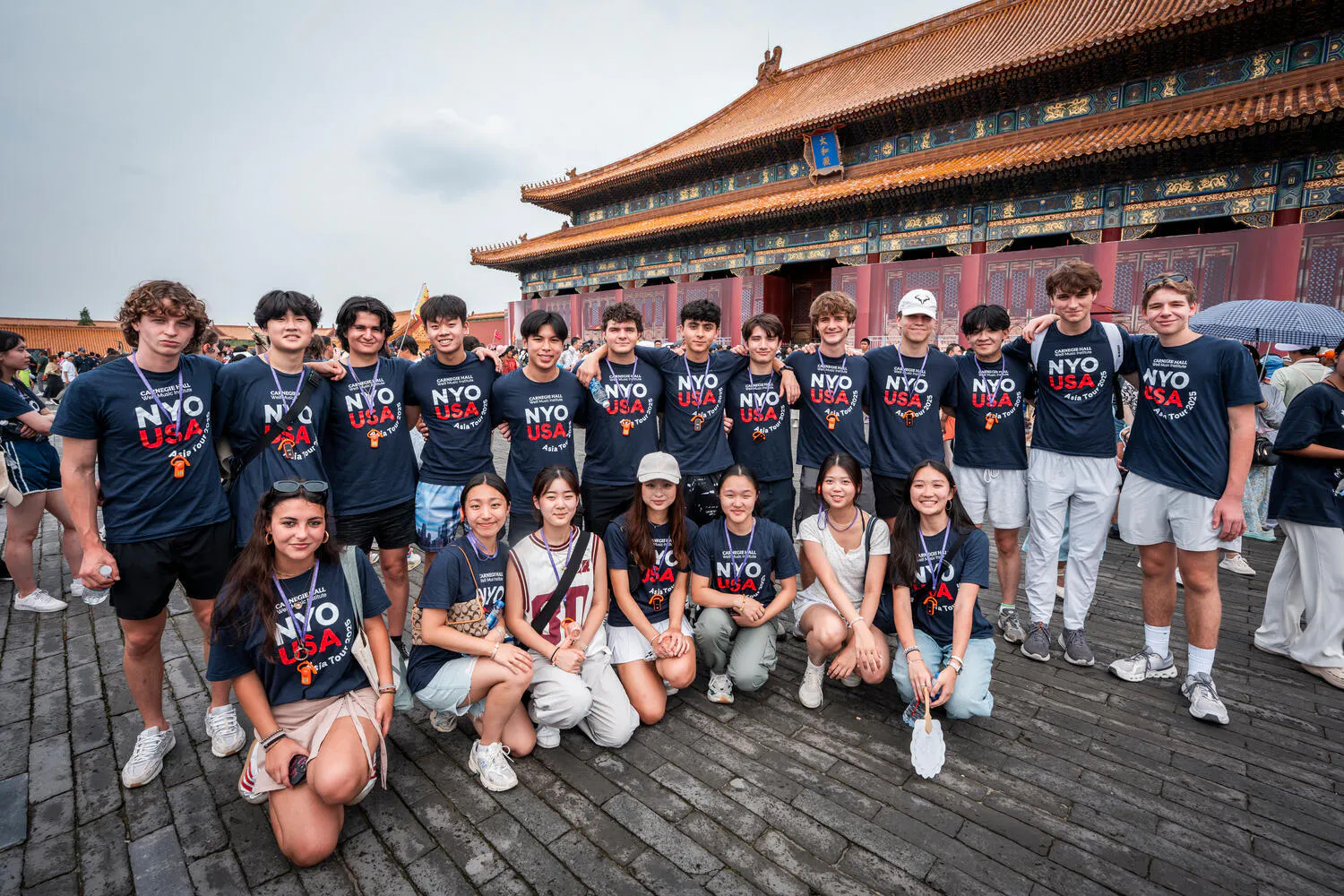 NYO-USA musicians wearing blue "NYO-USA" t-shirts pose before a pagoda-like building