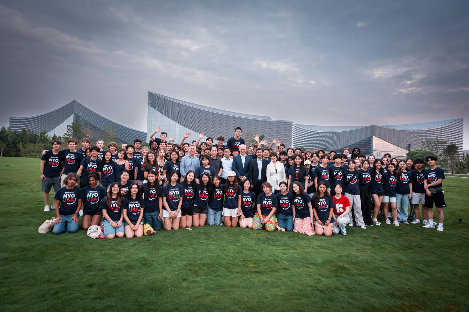 NYO-USA musicians pose together on a lawn before an outside amphitheater