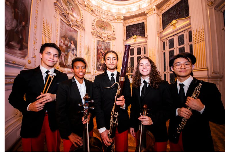 Young male and female musicians pose with their instruments wearing black blazers and red pants
